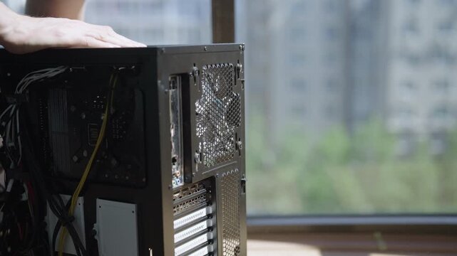 Close-up view of technician hand holding personal computer case blowing out dust with compressed air. Concept of motherboard, video card, rear fan during maintenance. Shooting in slow motion