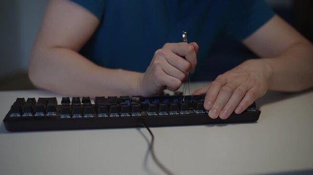 Closeup of man hands using special tool to remove keycaps from black mechanical keyboard for cleaning, maintenance, customization on white desk in home office setting. Shooting in slow motion