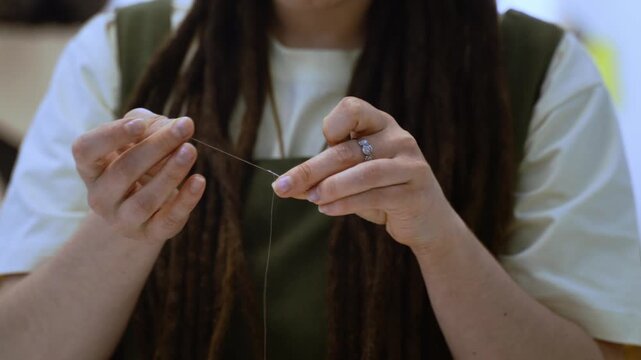 Female tailor with dreadlocks threading a needle for sewing in a workshop