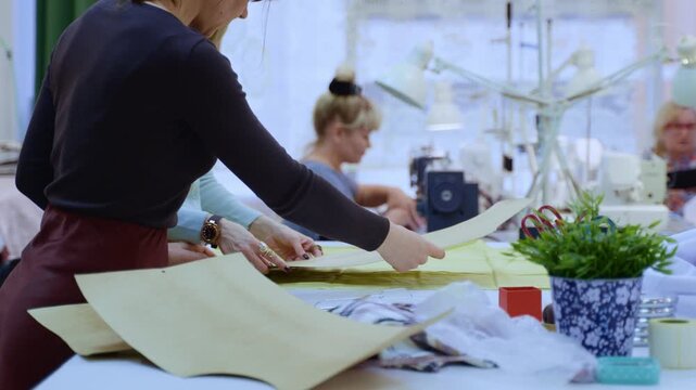 A dressmaker marks cut lines on textile using a paper pattern and chalk, running her marker along the edge of the template