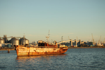 Fototapeta premium Rusting ship anchored in harbor at sunset