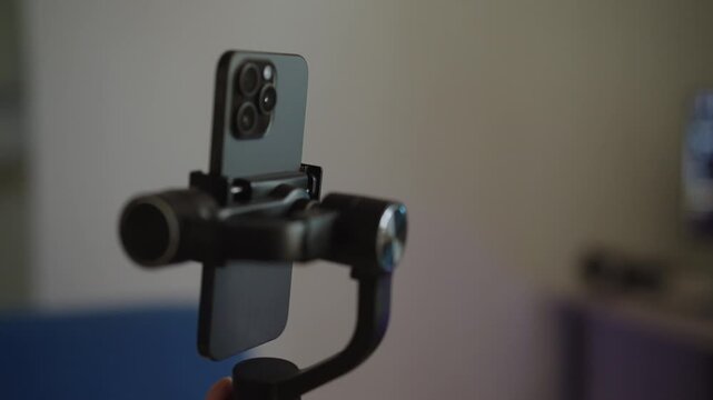 Professional filmmaker hand holding operating gimbal stabilizer with modern smartphone, creating smooth footage for vlogging, social media content creation, mobile videography, close-up, slow motion