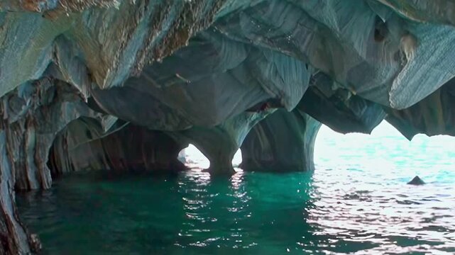 Witness sunlight dancing on pristine blue waters, flowing beneath ancient, sculpted marble arches within the glorious Marble Caves of Patagonia. A serene daytime exploration.