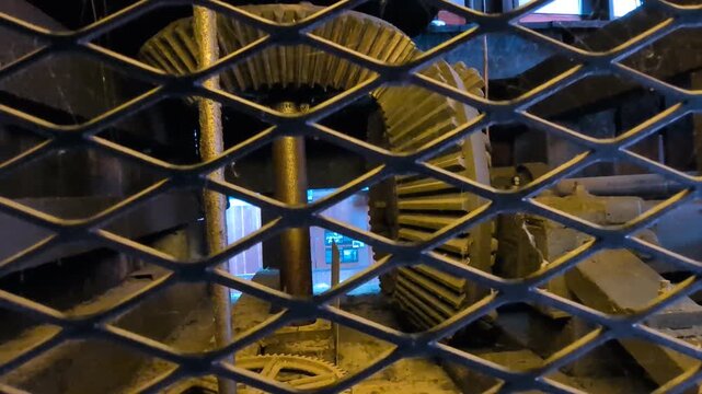Video close-up of historic metal gears and connecting rods behind a fence demonstrates the mechanical systems that once converted water power into productive mill operations.