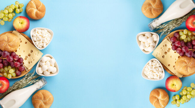 Jewish Shavuot holiday card concept. Dairy products, fruits, cheese, bread, milk bottle on blue background.