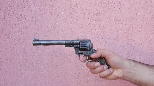 Close up footage of a hand operating a vintage style revolver toy pistol, rotating the cylinder with a finger before pulling the trigger. The spinning chamber mechanism is clearly visible in motion.