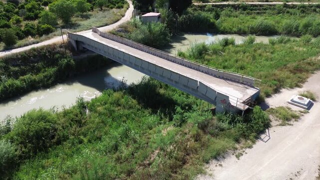 Aerial view of a concrete bridge crossing the rio Segura river surrounded by lush green vegetation and dirt roads representing rural infrastructure and peaceful outdoor nature travel scenery in Spain