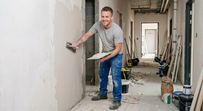 Smiling man plastering a wall in a corridor. Professional construction worker renovating a house