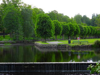 Fototapeta premium A beautiful scenic landscape in a city park in Finspång, Sweden, featuring a calm lake surrounded by green grass and natural vegetation. The peaceful environment reflects a typical Scandinavian park a
