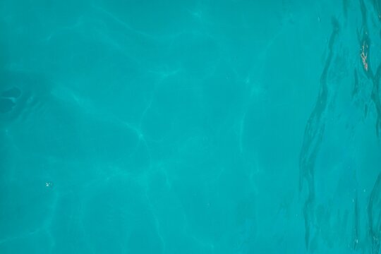 Blue turquoise water texture of the ocean sea with sun reflection for natural summer background and refreshing liquid surface concepts
