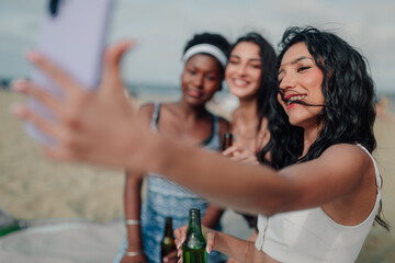 Fototapeta premium Diverse young women friends taking selfie at beach party enjoying summer carefree lifestyle with drinks