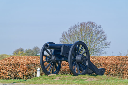Historic black cannon on grassy mound with clear blue sky and trees in background