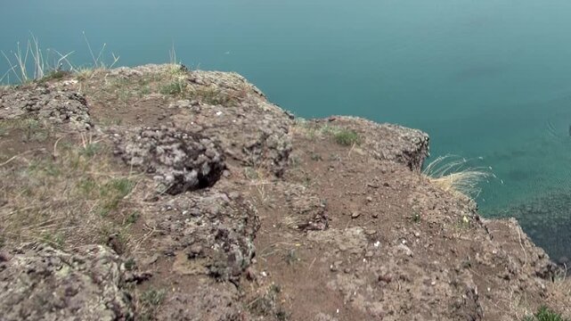 A tiny dweller blends with the sun-drenched rocky bluff above the clear, azure expanse of Khuvsgul Lake. This serene moment unfolds high above the waters in magnificent Mongolia.