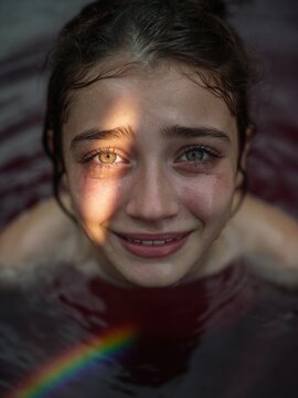 Emotional young woman with tears in reflective water illuminated by dramatic sunlight and rainbow prism