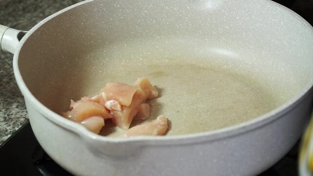 Close up of hands putting raw diced chicken breast into a hot frying pan with oil