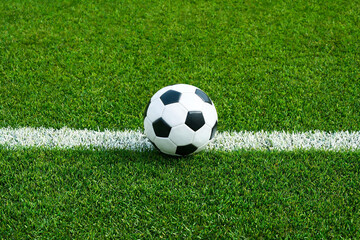 Fototapeta premium Balón de fútbol clásico sobre césped verde impecable colocado exactamente en la línea blanca del campo de juego. Concepto de saque inicial, reglas del juego, comienzo del partido y torneo.
