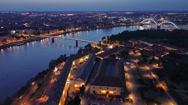 Aerial view of cityscape of Novi Sad at night, with illuminated bridges over Danube river and Petrovaradin fortress, Serbia, 4k