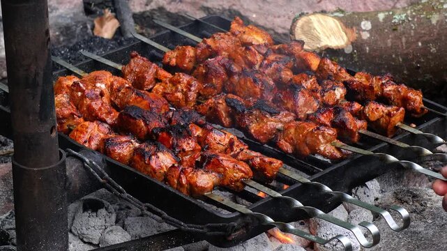 Small pieces of meat are frying over an open campfire, with a browned surface and a rustic outdoor cooking atmosphere. The scene highlights the heat, smoke, and natural setting of meat being cooked di
