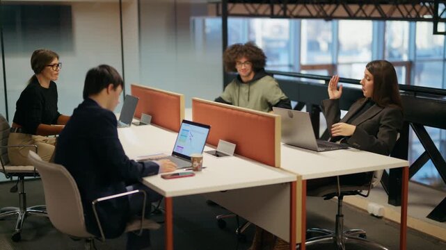 Young professionals diligently work on their laptops in a modern office environment. Coworkers are engaged in their tasks at individual workstations