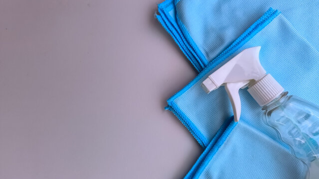 Hand holding a detergent spray bottle ready for cleaning next to blue rags on a blue surface.