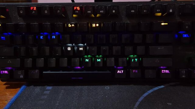 High angle view of a PC gaming setup in a dark room featuring a mechanical keyboard and mouse with vibrant RGB LED backlit lighting effects.