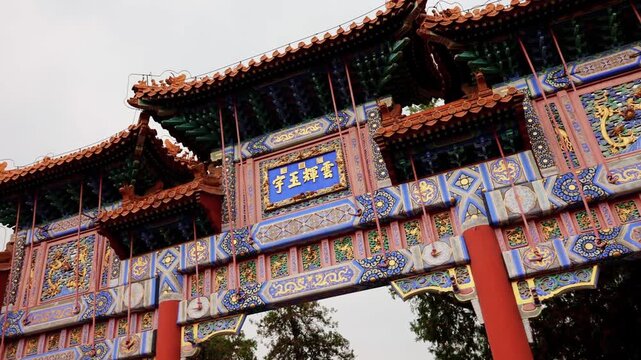 Richly decorated imperial archway with painted beams in Summer Palace. View of layered rooflines, carved panels, Chinese characters and vivid blue gold colors under cloudy sky, Beijing, China, 4k