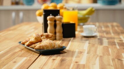 Kitchen with wooden breakfast table with pastry and fruits in empty home, natural light enhances...