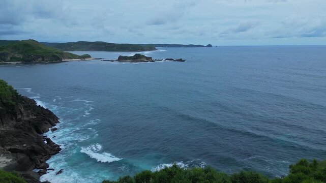 Wide Drone Shot Rugged Coastline And Ocean Under Moody Sky Deep Blue Water, Crashing Waves On Basalt Cliffs, Distant Islets, Cool Tones, Atmospheric Survey Footage, Bukit Merese, Lombok, Tanjung Ann