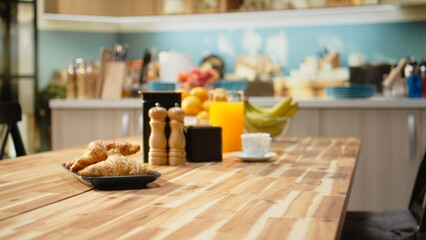 Empty breakfast table in a modern kitchen featuring croissants on plate, natural light fills the...