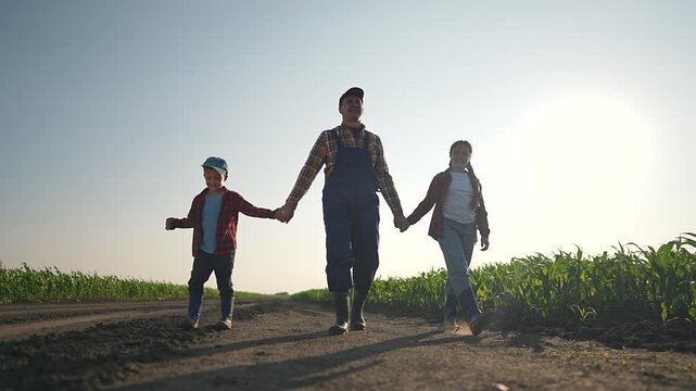 Father, son, and daughter walk hand in hand across a sunny farm field. Family enjoying outdoor time together, appreciating the rural environment. Exploring agriculture and spending time outdoors.