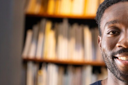 Adult African American man smiling, wearing dark crewneck tee in library with bookshelf, copy space
