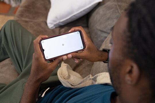 Adult African man holding phone showing crosshair markers, sitting on brown sofa with beige towel