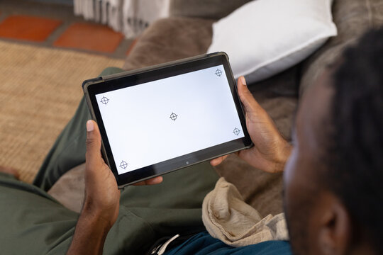 Tablet is resting on brown sofa with white pillow and beige throw, rug and tile visible