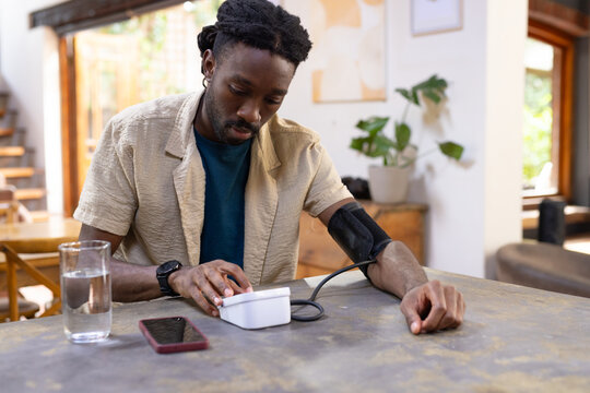 Man sitting at wooden table pressing blood pressure monitor button with red smartphone nearby
