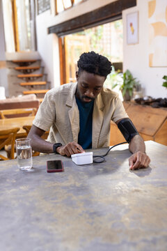 African American man checking blood pressure at table in beige shirt with cuff, using white monitor