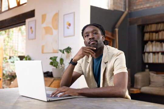 Man sitting at wooden table in bright loft using open laptop wearing beige overshirt wristwatch