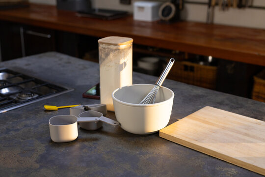 White mixing bowl holding metal whisk is sitting on dark counter with flour canister
