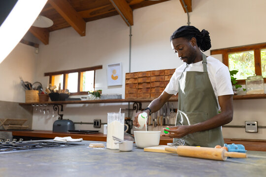 African man in green apron preparing batter on kitchen countertop with mixing bowl, copy space