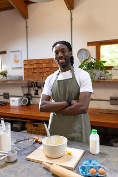 Man wearing olive-green apron stirring batter in mixing bowl with whisk in rustic kitchen