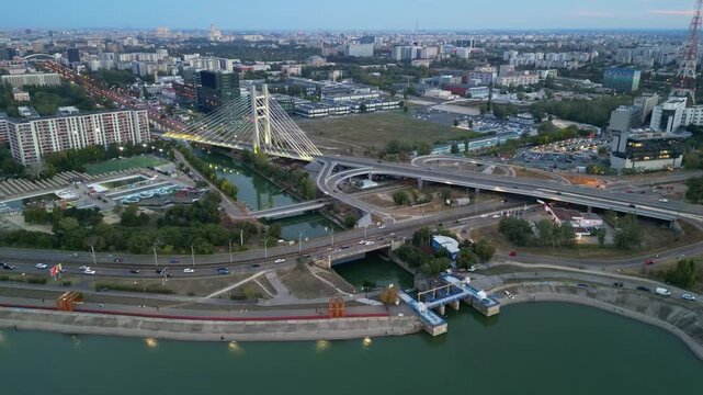 Cinematic high angle night view of the illuminated Ciurel bridge in Bucharest, Romania. Modern cable-stayed overpass surrounded by vibrant city traffic lights.