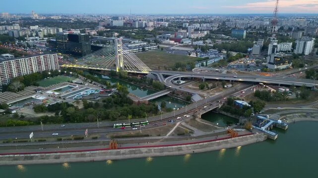 Cinematic high angle night view of the illuminated Ciurel bridge in Bucharest, Romania. Modern cable-stayed overpass surrounded by vibrant city traffic lights.