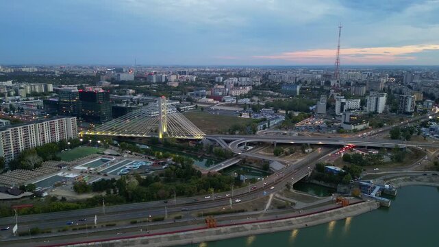 Cinematic high angle night view of the illuminated Ciurel bridge in Bucharest, Romania. Modern cable-stayed overpass surrounded by vibrant city traffic lights.