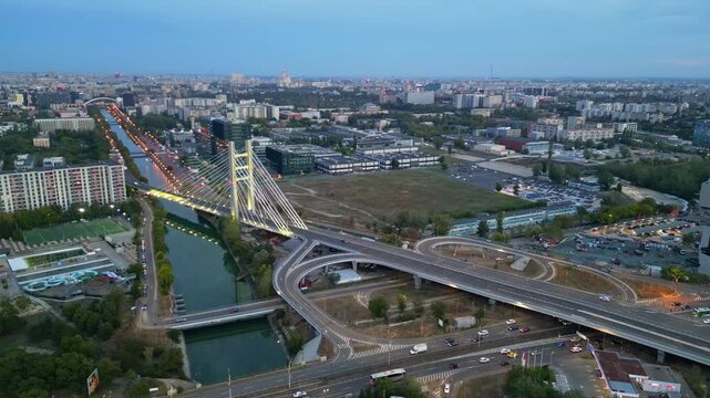 Cinematic high angle night view of the illuminated Ciurel bridge in Bucharest, Romania. Modern cable-stayed overpass surrounded by vibrant city traffic lights.
