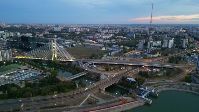 Cinematic high angle night view of the illuminated Ciurel bridge in Bucharest, Romania. Modern cable-stayed overpass surrounded by vibrant city traffic lights.