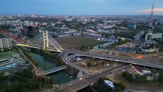 Cinematic high angle night view of the illuminated Ciurel bridge in Bucharest, Romania. Modern cable-stayed overpass surrounded by vibrant city traffic lights.