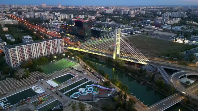Cinematic high angle night view of the illuminated Ciurel bridge in Bucharest, Romania. Modern cable-stayed overpass surrounded by vibrant city traffic lights.