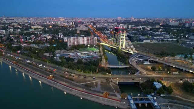 Cinematic high angle night view of the illuminated Ciurel bridge in Bucharest, Romania. Modern cable-stayed overpass surrounded by vibrant city traffic lights.