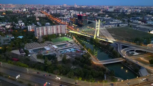 Cinematic high angle night view of the illuminated Ciurel bridge in Bucharest, Romania. Modern cable-stayed overpass surrounded by vibrant city traffic lights.