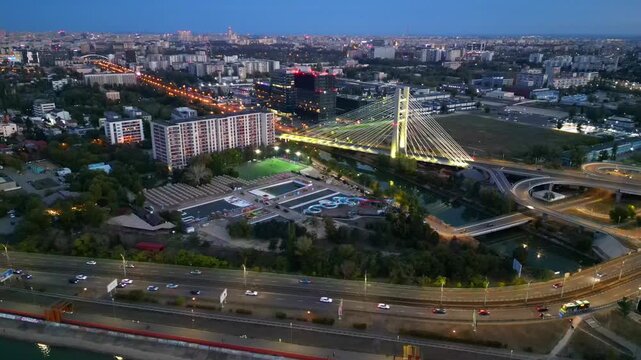 Cinematic high angle night view of the illuminated Ciurel bridge in Bucharest, Romania. Modern cable-stayed overpass surrounded by vibrant city traffic lights.