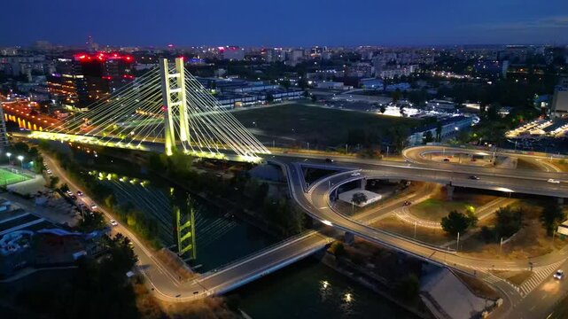 Cinematic high angle night view of the illuminated Ciurel bridge in Bucharest, Romania. Modern cable-stayed overpass surrounded by vibrant city traffic lights.